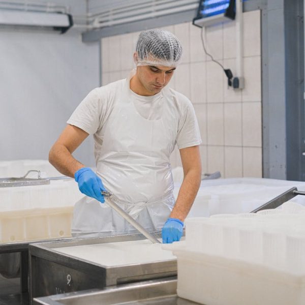 Man in a dairy factory wearing protective gear, handling a ladle. Industrial setting.